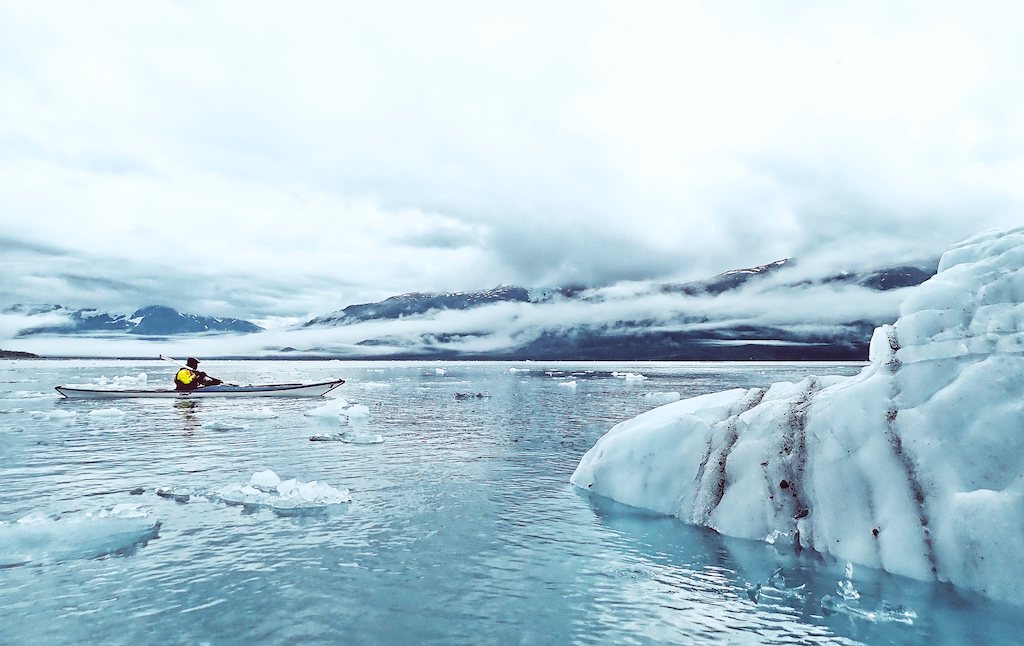 A kayaker rowing alongside some blocks of ice at Surprise Glacier in Alaska, where global warming is accelerating the melting of the glaciers at a high speed.