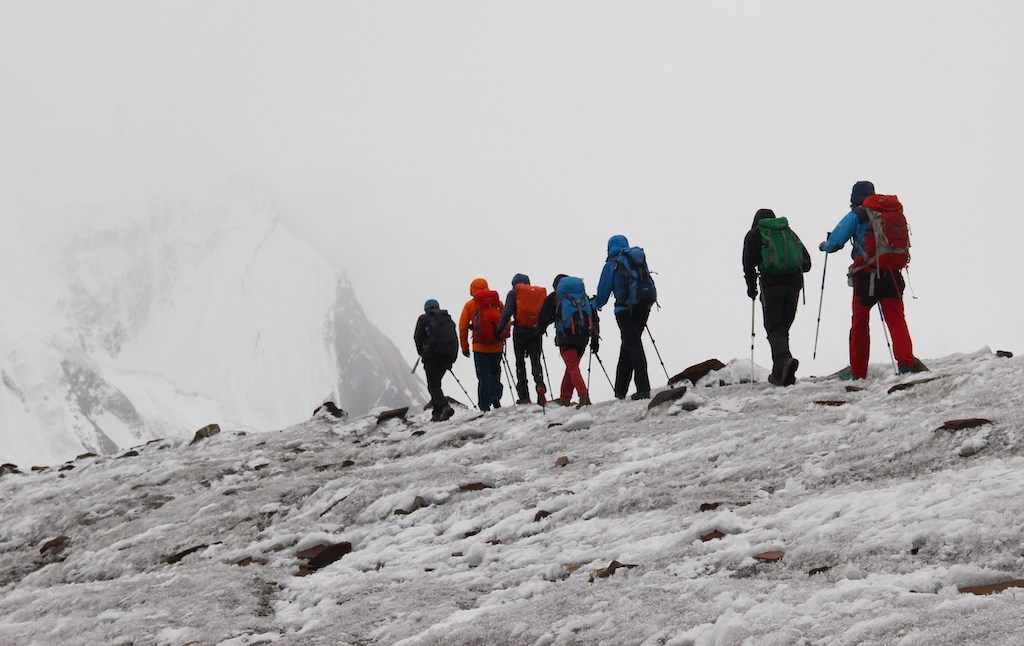 A group of warmly dressed hikers with a trekking backpack on the Vigne Glacier, along a multi-day trip.