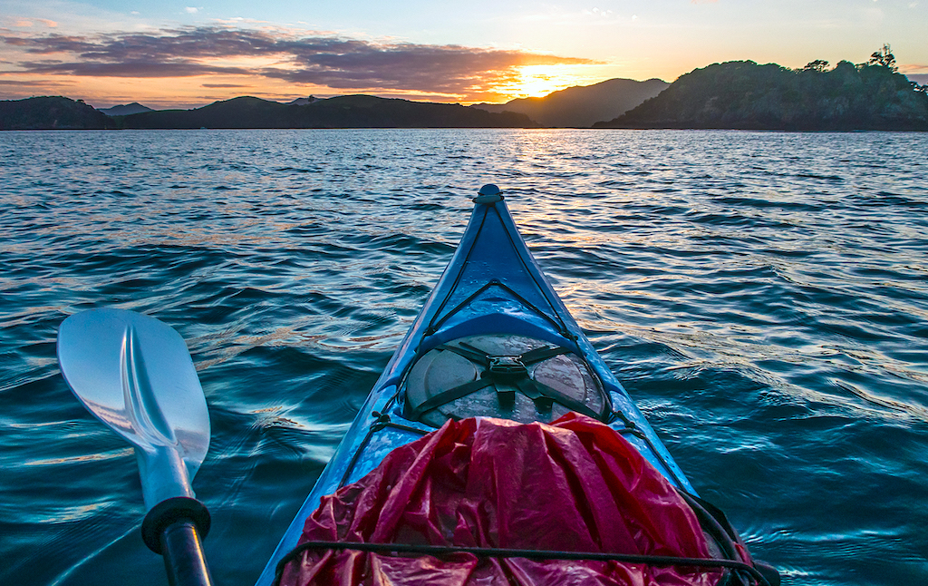 The bow of a kayak, alongside the blade of a kayak paddle, in the waters of the Bay of Islands (New Zealand).